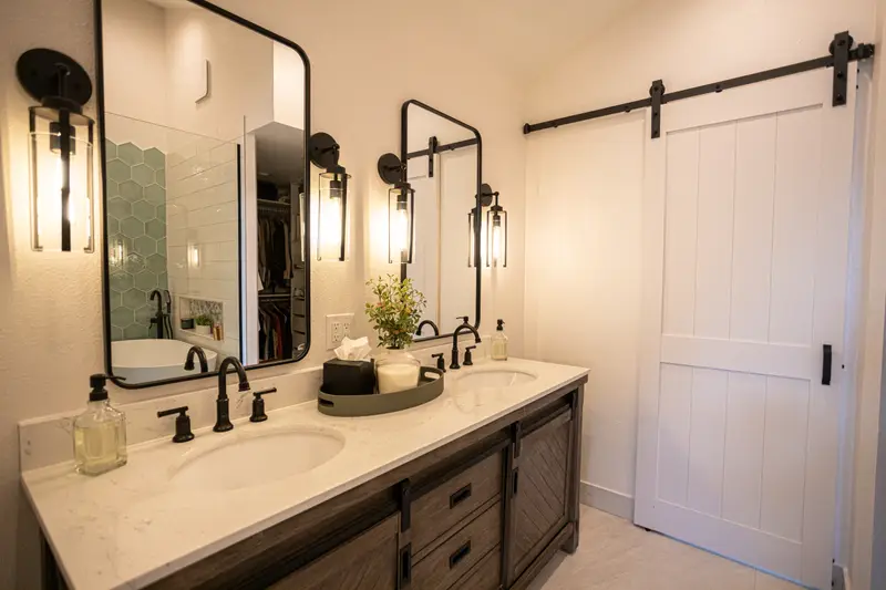 Primary bathroom in Erie, Colorado with a double vanity, black fixtures and sconces, black-framed mirrors and a white sliding barn door