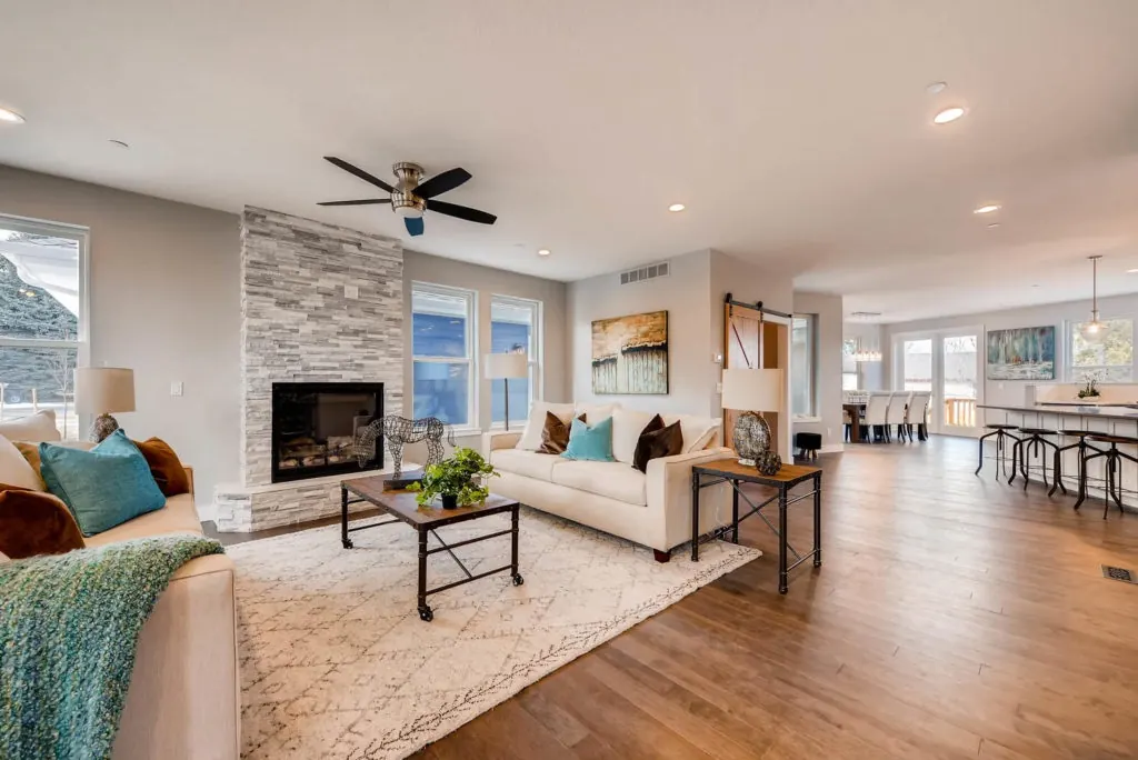 Open-concept main floor of a custom home in Arvada, Colorado, with a stone fireplace, wide-plank hardwood floors and the kitchen beyond