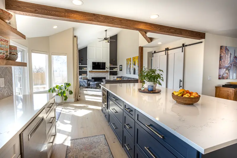 Remodeled kitchen in Superior, Colorado with a navy island, white counters and wood ceiling beams, open to a vaulted living room